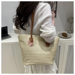Detail of woven straw tote bag featuring brown leather straps and pink mesh bow charm