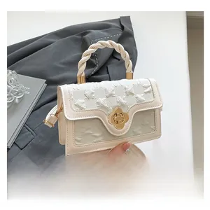 Detail of cream crossbody bag with floral gold clasp and woven handle on grey blazer