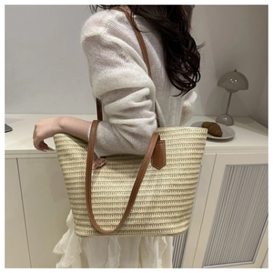 Detail of straw woven tote bag with brown leather straps and pink butterfly charm