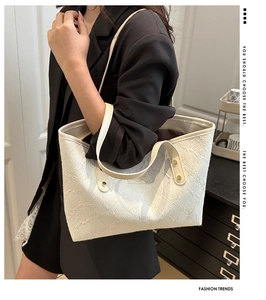 Close-up of a white textured tote bag with golden studs on strap and leather brand label