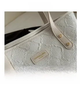 Close-up of white tote bag featuring floral embroidery and textured leather with gold rivets
