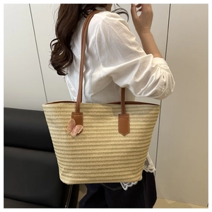 Close-up of beige straw tote bag with brown leather straps and pink butterfly embroidery