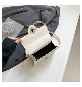 Detail of cream white leather mini bag featuring a gold clover clasp and thin shoulder strap