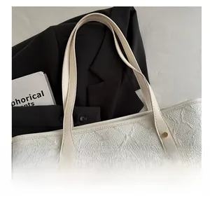 Close-up of geometric embossed cream tote bag with leather straps and gold stud accents