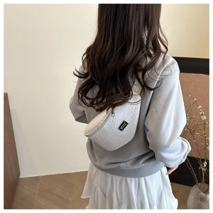 Detail of white woven texture on crossbody chest bag worn by a model in a cozy room