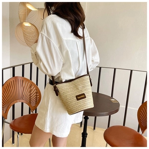 Modella che indossa una borsa a secchiello in paglia con finiture in pelle in un caffè