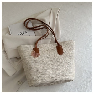Detail of woven straw tote bag featuring brown straps and a pink mesh butterfly charm