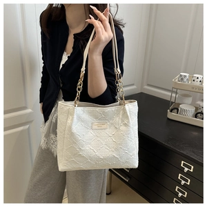 Detail of off-white canvas tote bag featuring 3D embossed texture and gold chain strap