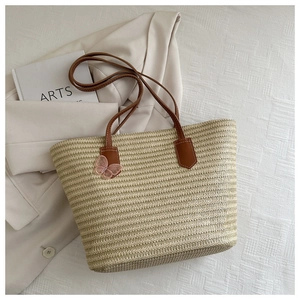 Detail of straw tote bag with brown faux leather handles and a pink butterfly charm