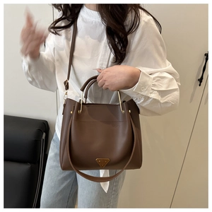 Detail view of brown leather tote bag with gold triangular plaque and metal handle