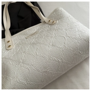 Detail of white pleated tote bag featuring delicate floral embroidery and branded fabric tag