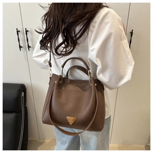Brown leather bucket bag detail with golden triangle metal logo shown on model