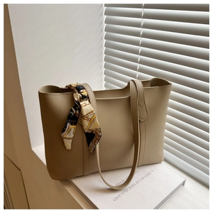 Detail of a beige leather tote bag featuring a silk scarf bow and long shoulder straps
