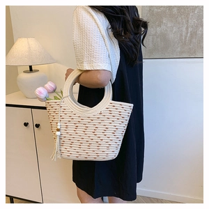 Détail du sac seau en paille tissée avec pois marrons et pompon en coton sur la lanière