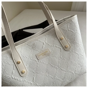 Detail of white tote bag featuring 3D floral embroidery and gold metal brand plaque