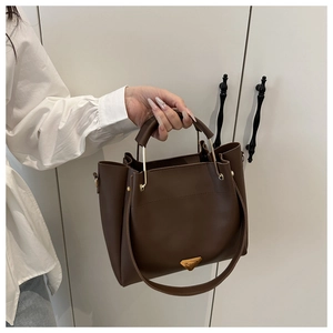 Detail view of large dark brown tote bag with gold metal plaque and dual shoulder straps