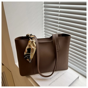 Detail of a brown leather tote bag decorated with a vintage patterned silk scarf on handle