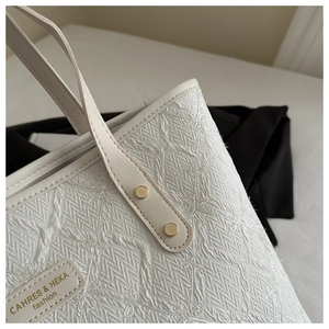 Close-up of white tote bag with floral embroidery, textured fabric, and gold rivet details