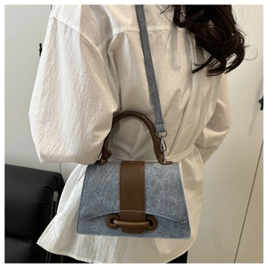 Detail view of denim texture handbag with brown leather trim and metal ring closure