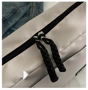 Détail de la fermeture éclair métallique et du cordon tressé noir sur un sac beige