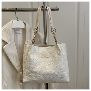 Close-up of white embossed tote bag featuring geometric patterns and gold chain handle