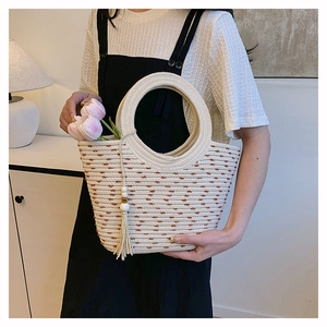 Détail du sac seau en paille tressée avec pompon en perles de bois et anse ronde