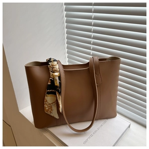 Detail of a brown leather tote bag with a patterned silk scarf on a book