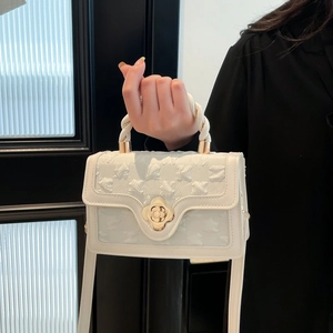 Detail of white embossed fabric handbag with twisted rope handle and gold floral clasp