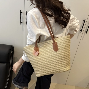 Large beige woven straw tote bag with brown straps and pink butterfly charm accessory