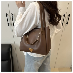 Detailed view of brown bucket bag with gold triangular metal plate and rivet handles