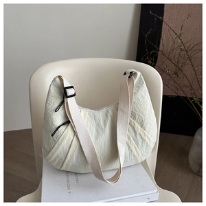 Vue détaillée du sac demi-lune beige en tissu texturé sur une chaise blanche