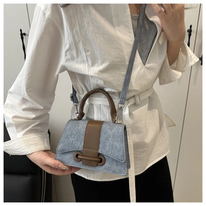 Detail of blue denim square bag with brown leather trim worn by a model in lifestyle setting