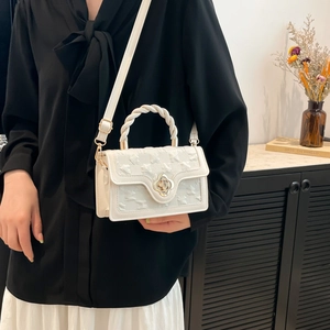 Detail of white textured square bag featuring flower twist lock and spiral handle design