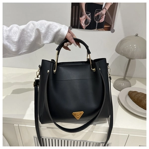 Detail of black tote bag with golden circular metal handle and triangular metal logo plate