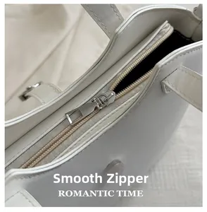 Detailed macro view of the smooth metal zipper and leather texture on a white handbag