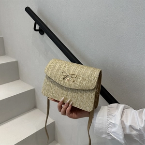 Détail d'un sac bandoulière en paille tressée avec fermoir nœud doré et bandoulière fine