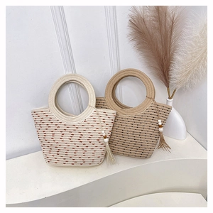 Détail de sacs seaux en paille avec poignées anneaux et pompons au style estival