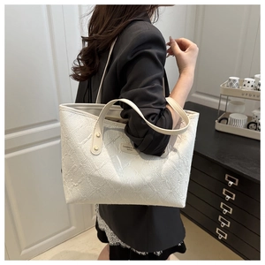 Detail of white tote bag featuring woven texture and silver brand plaque on leather