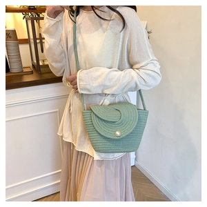 Gros plan d'un sac bandoulière tressé vert avec une grande boucle perle sur le rabat
