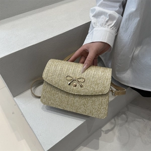 Détail du sac bandoulière en paille tressée avec nœud doré et sangle en cuir