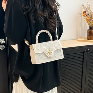 Close-up of quilted cream handbag featuring a golden floral twist lock and woven handle