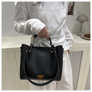 Close-up of black matte leather tote bag featuring gold hardware and triangular metal plaque