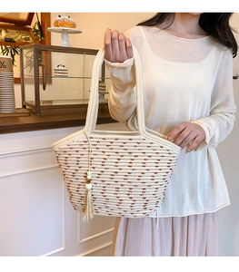 Close-up of woven straw tote bag with brown accents and tassel detail in a cafe