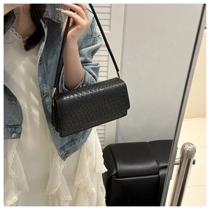 Detail of black woven texture shoulder bag with gold metal hardware in a casual outfit