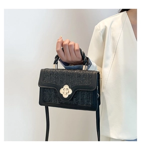 Detail of black woven crossbody bag with golden flower twist lock and twisted handle