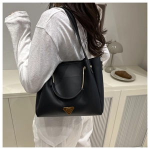 Detail shot of a sleek black tote bag featuring a gold triangle logo and metallic handle