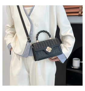 Detail of black woven shoulder bag featuring a gold floral clasp and adjustable strap