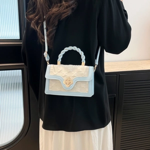Detail of light blue crossbody bag featuring braided handle and golden flower clasp
