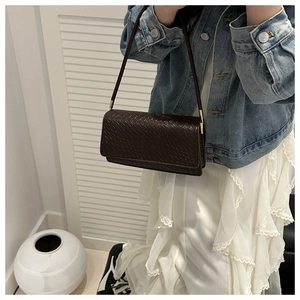 Detail of dark brown woven texture on a rectangular shoulder bag with gold buckle hardware