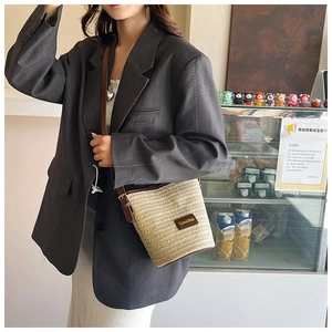 Dettaglio borsa a secchiello in paglia beige con finiture in pelle marrone scuro
